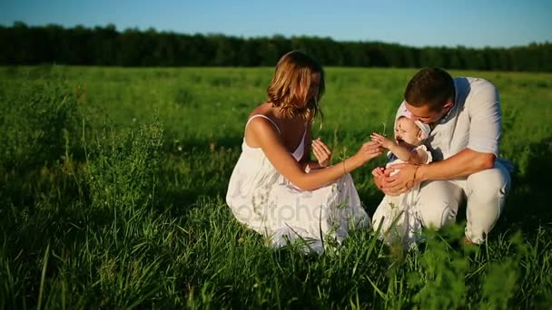 Gelukkige familie. Vader moeder en een meisje, wandelen in een veld gekleed in het wit onder de stralen van de ondergaande zon — Stockvideo