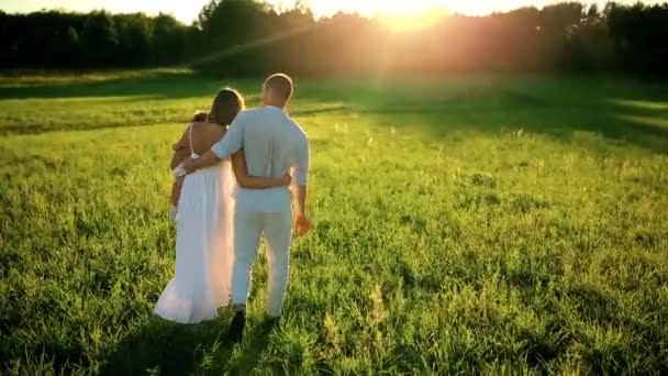 Una famiglia felice. Papà mamma e una bambina, camminando in un campo vestito di bianco sotto i raggi del sole al tramonto — Video Stock