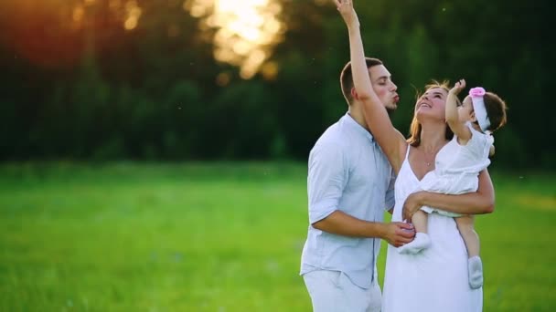 Familia joven feliz con niño caminando en el campo de verano. Madre sana, padre e hija pequeña disfrutando de la naturaleza juntos, al aire libre. Puesta de sol . — Vídeos de Stock