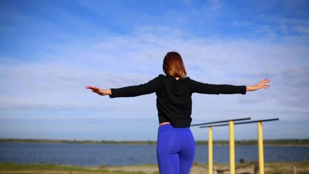 La chica en la sudadera con capucha, llega al río, se quita la chaqueta y realiza estiramiento del cuello y los hombros . — Vídeos de Stock