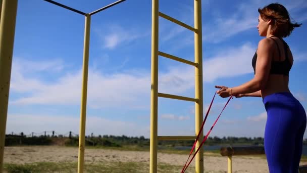 Mavi tozluk ile şirin sportif esmer gerilebilir elastik ile sokakta el kaslarını güçlendirmek için egzersizler yapın. Açık havada egzersiz. — Stok video