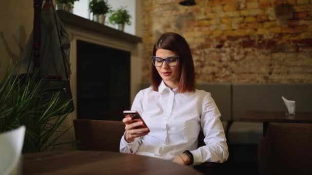 Charming woman with beautiful smile reading good news on mobile phone during rest in coffee shop, happy Caucasian female watching her photo on cell telephone while relaxing in cafe during free time. — Stock Video