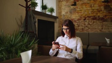 Güzel gülümseme kafede, onun resmi hücre telefon için serbest zaman sırasında kafede dinlenirken izlerken mutlu beyaz kadın dinlenme sırasında cep telefonu üzerinde iyi haber okuma ile büyüleyici kadın.