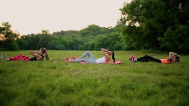 Abs kızlarına hissediyor. Grup yaz Park açık havada, yan görünüm yeşil çimenlerin üzerinde fiziksel egzersizleri yapıyor spor genç atletik insan