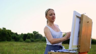 Rüzgarda geliştirir uzun saçlı genç bir kadın boya resim üzerine yağlıboya, şövale üzerinde duruyor. Bayan açık bir havada, o hayattan çizer