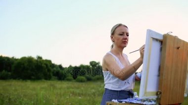 Rüzgarda geliştirir uzun saçlı genç bir kadın boya resim üzerine yağlıboya, şövale üzerinde duruyor. Bayan açık bir havada, o hayattan çizer