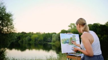 genç sanatçı Resim Resim fırçaları ve romantik göl ve arka plan kentsel binalarda oturan renkleri ile parkta. Ultra geniş açılı görünüş