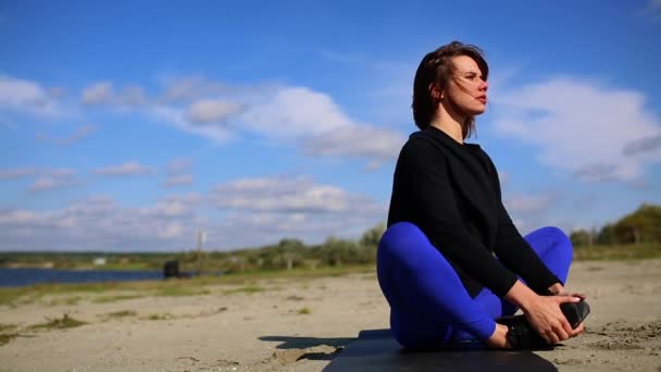 Jeune femme faisant de l'exercice de yoga sur la plage de sable d'été au coucher du soleil, séance d'entraînement . — Video