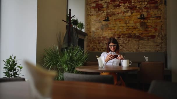 Šťastná mladá žena sedí v kavárně textilie na svého chytrého telefonu — Stock video