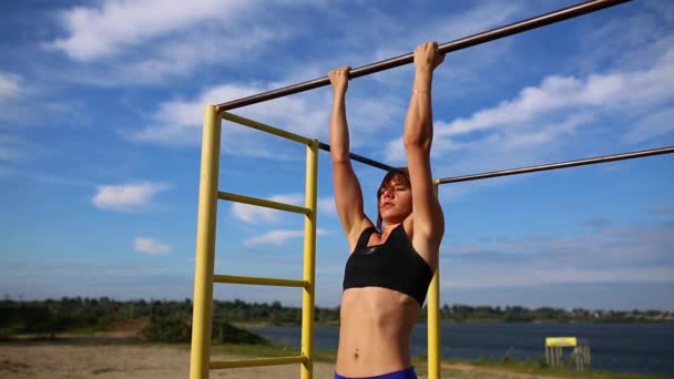Sport flicka utför en chin-up nära floden på bakgrund av blå himmel. — Stockvideo