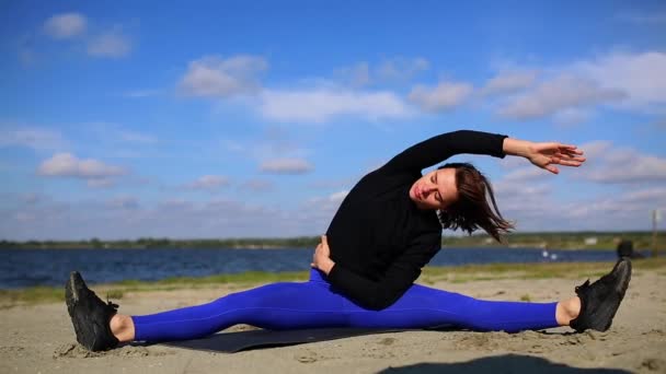 Дівчина на річці Банк виконує розтягування та розслаблення м'язів після важкого тренування. Фітнесу та йоги за межами біля пляжу. — стокове відео