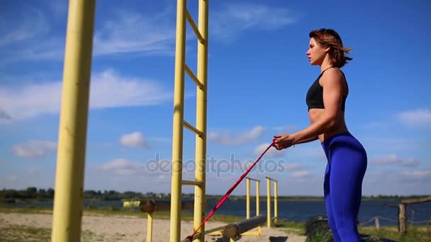 Mavi tozluk ile şirin sportif esmer gerilebilir elastik ile sokakta el kaslarını güçlendirmek için egzersizler yapın. Açık havada egzersiz. — Stok video