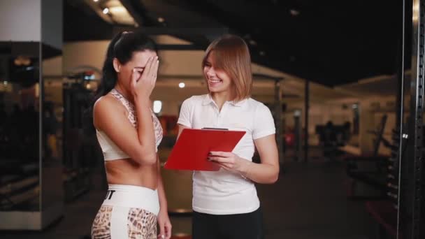 Vrouwelijke persoonlijke trainer in gesprek met een client van de vrouw in een sportschool met behulp van een tablet voor notities. — Stockvideo