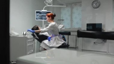 Mavi eldiven ve Beyaz önlük kadın doktor hastayı sandalyeye yaklaşımlar ve x-ışını ve araçlarını kullanarak ağız boşluğu dişinde diş hekimi olup olmadığını denetler. Kız hasta.