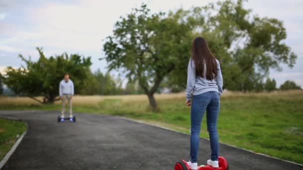 若い男と公園でホバーボードに乗って女。コンテンツの技術。新しい動き。デュアル ホイールのを分散電気スケート ボード スマート自己を閉じます。屋外の電気スクーターに. — ストック動画