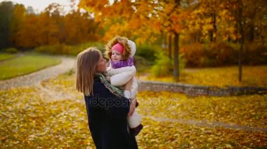 Sonbahar, ne zaman anne ve gülerek ve gülümseyerek akçaağaç yaprakları ile oynayan kız çevresinde sarı yapraklar. Anne hugs ve kızımla sonbaharda çalış. Bokeh ve güneş ışığı.