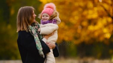 Sonbahar, ne zaman anne ve gülerek ve gülümseyerek akçaağaç yaprakları ile oynayan kız çevresinde sarı yapraklar. Anne hugs ve kızımla sonbaharda çalış. Bokeh ve güneş ışığı.