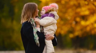 Sonbahar, ne zaman anne ve gülerek ve gülümseyerek akçaağaç yaprakları ile oynayan kız çevresinde sarı yapraklar. Anne hugs ve kızımla sonbaharda çalış. Bokeh ve güneş ışığı.