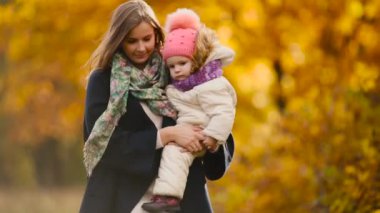 Sonbahar, ne zaman anne ve gülerek ve gülümseyerek akçaağaç yaprakları ile oynayan kız çevresinde sarı yapraklar. Anne hugs ve kızımla sonbaharda çalış. Bokeh ve güneş ışığı.