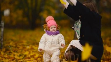 Sonbahar, ne zaman anne ve gülerek ve gülümseyerek akçaağaç yaprakları ile oynayan kız çevresinde sarı yapraklar. Anne hugs ve kızımla sonbaharda çalış. Bokeh ve güneş ışığı.