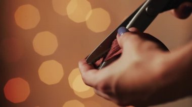 Eller, Close-Up sevdiklerinize Noel için el yapımı Hediyelik üretimi için şerit kesin. Arka plan bulanık ışıklar çelenk. Bokeh.