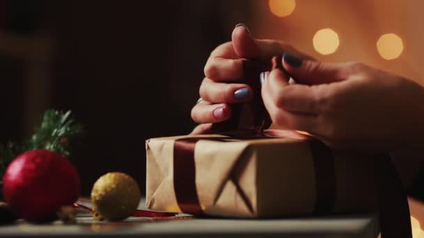 Close-up op de achtergrond van Kerstmis licht womens handen koppelverkoop het lint op de gave van kraftpapier. De achtergrond is wazig in bokeh. — Stockvideo