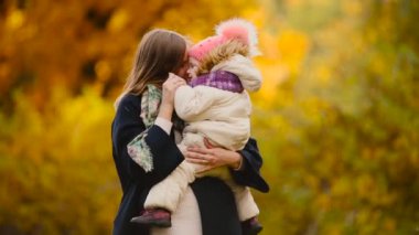 Sonbahar, ne zaman anne ve gülerek ve gülümseyerek akçaağaç yaprakları ile oynayan kız çevresinde sarı yapraklar. Anne hugs ve kızımla sonbaharda çalış. Bokeh ve güneş ışığı.