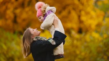 Sonbahar, ne zaman anne ve gülerek ve gülümseyerek akçaağaç yaprakları ile oynayan kız çevresinde sarı yapraklar. Anne hugs ve kızımla sonbaharda çalış. Bokeh ve güneş ışığı.