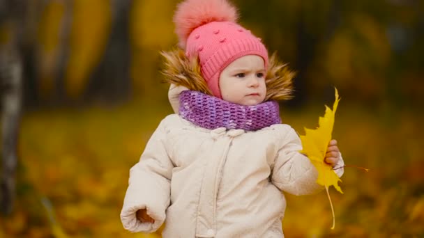 Närbild porträtt av lilla flickan står med ett lönnlöv och tittar mot kameran ler och pratar med mamma. — Stockvideo