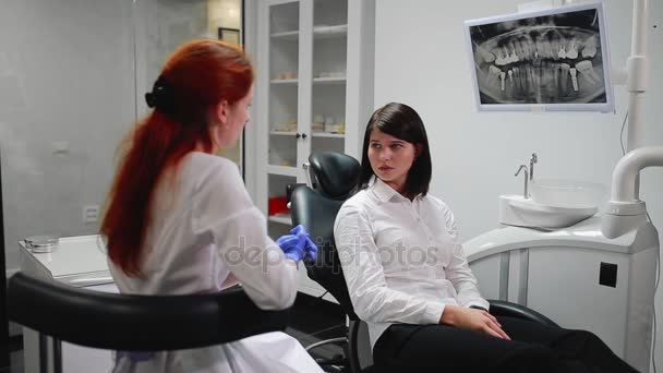 Vacker flicka konsulterat en tandläkare i hans kontor boll på bräss av smärtan pekar på tänderna. Vita, sterila läkare kontor. Skärmen visar en röntgenbild av tanden i munhålan — Stockvideo
