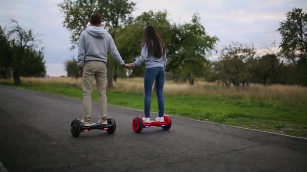 Ung man och kvinna rider på Hoverboard i parken. innehåll teknik. en ny rörelse. Stäng av dubbla hjul själv Balancing Electric Skateboard Smart. på elektriska scooter utomhus. — Stockvideo