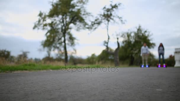 Giovane uomo e donna che cavalcano sull'Hoverboard nel parco. tecnologie dei contenuti. un nuovo movimento. Close Up di doppia ruota auto bilanciamento Skateboard elettrico intelligente. su scooter elettrico all'aperto . — Video Stock