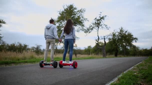 Jovem homem e mulher montando no Hoverboard no parque. tecnologias de conteúdo. um novo movimento. Close Up of Dual Wheel Auto balanceamento skate elétrico inteligente. em scooter elétrico ao ar livre . — Vídeo de Stock