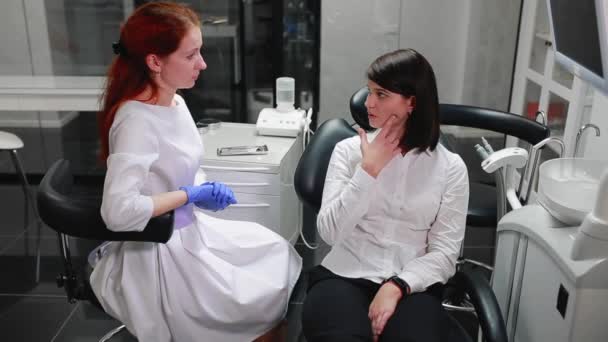 Όμορφο κορίτσι διαβουλεύσεις με έναν οδοντίατρο του γραφείου μπάλα στον θύμο αδένα από τον πόνο που δείχνει τα δόντια της. Γραφείο ιατρών άσπρο, αποστειρωμένο. — Αρχείο Βίντεο