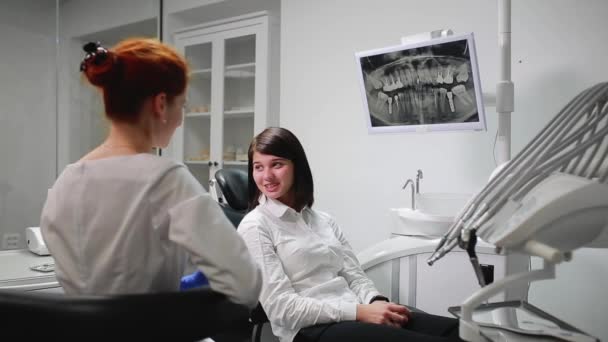 Bella ragazza consultato un dentista nel suo studio palla sul timo del dolore che punta i denti. Studio medico bianco e sterile. Lo schermo mostra una radiografia del dente nella cavità orale — Video Stock