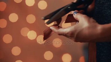 Eller, Close-Up sevdiklerinize Noel için el yapımı Hediyelik üretimi için şerit kesin. Arka plan bulanık ışıklar çelenk. Bokeh.