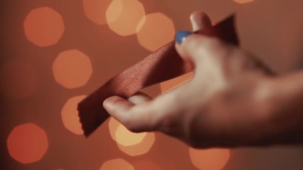 Közeli kép a női kéz, vágni a szalagot, kézzel készített ajándék karácsonyra gyártásához a szeretteit. A háttérben a világítás homályos koszorúkat. Bokeh. — Stock videók