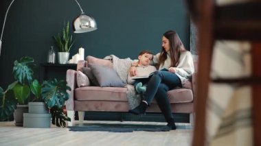 Evinizin oturma odasında kanepede oturan güzel genç anne oğlu kulak bir hikaye okur ve küçük çocuk okumayı öğrenmek.