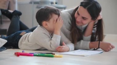Oğlumla işaretleri ile ailesi tasvir kağıt üzerine çizim yerde yatarken bir sıcak kazaklı güzel genç anne. Çocuk çizmeyi öğrenir. Yakın çekim