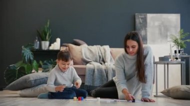 Annesi beyaz iç evinin bir çocukla katta oturan boya can açıldı ve parmaklarını boya daldırma ve elle kağıt üzerinde çizin. Mutlu bir aile.