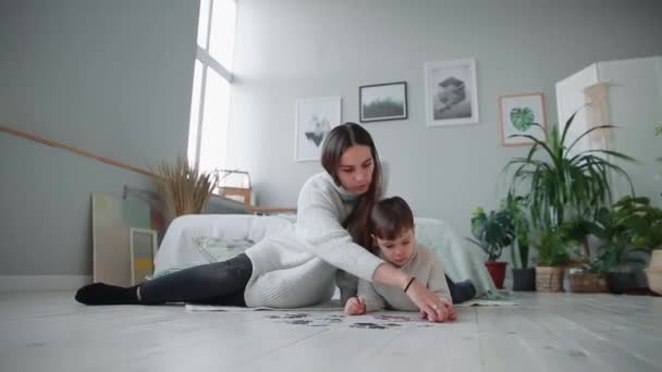 Mutter mit Kind im weißen Inneren seines Hauses, um das Puzzle zusammen mit seinem kleinen Sohn zu sammeln. glückliche Familie, Lernspiele. — Stockvideo