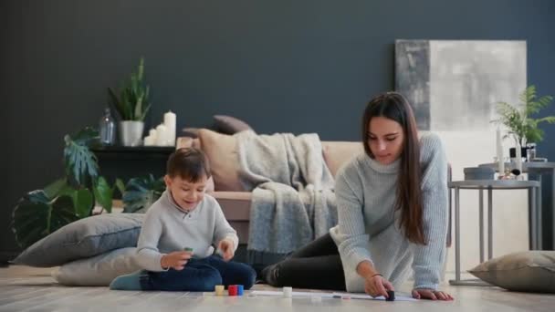 Madre con un niño en el interior blanco de su casa se abrió la pintura puede sentarse en el suelo y sumergir los dedos en pintura y dibujar en papel con las manos. Familia feliz . — Vídeos de Stock