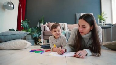 Oğlumla işaretleri ile ailesi tasvir kağıt üzerine çizim yerde yatarken bir sıcak kazaklı güzel genç anne. Çocuk öğrenir çizmek için.