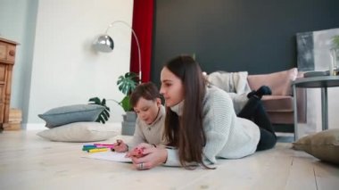 Oğlumla işaretleri ile ailesi tasvir kağıt üzerine çizim yerde yatarken bir sıcak kazaklı güzel genç anne. Çocuk öğrenir çizmek için.