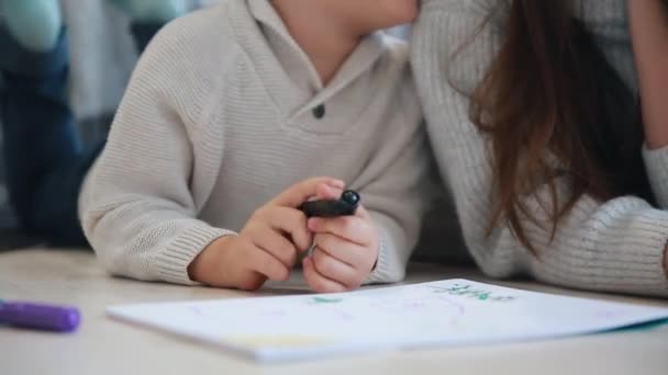 Belle jeune mère dans un pull chaud couché sur le sol avec mon fils dessin avec des marqueurs sur papier représentant sa famille. L'enfant apprend à dessiner. Gros plan — Video