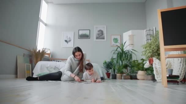 Moeder met een kind in het witte interieur van zijn huis te verzamelen van de puzzel samen met zijn jonge zoon. Gelukkige familie, educatieve spelletjes. — Stockvideo