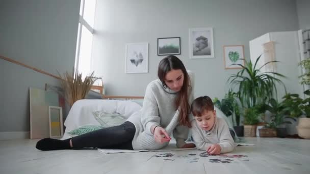 Madre con un niño en el interior blanco de su casa para recoger el rompecabezas junto con su hijo pequeño. Familia feliz, juegos educativos . — Vídeos de Stock