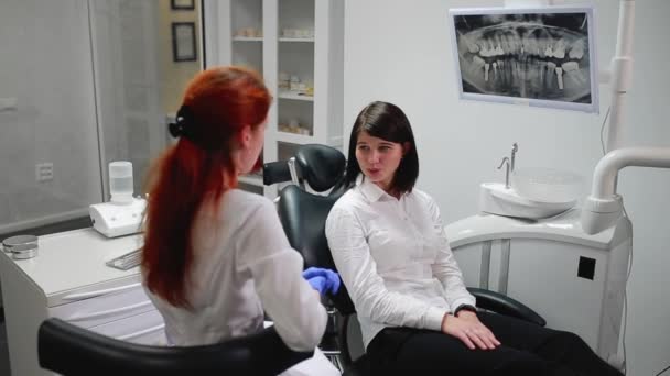 Bella ragazza consultato un dentista nel suo studio palla sul timo del dolore che punta i denti. Studio medico bianco e sterile. Lo schermo mostra una radiografia del dente nella cavità orale — Video Stock