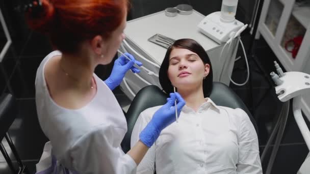 Woman doctor examines a patient in a white shirt in a white sterile office in blue gloves. Conducts the oral examination. — Stock Video