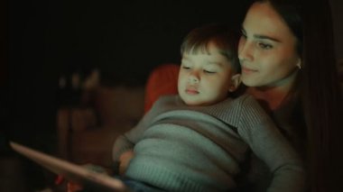 Güzel kadın anne evine oğlu ile çizgi tablet dokunmatik ekranda izlerken onun kucağına bir sandalyede oturuyor.